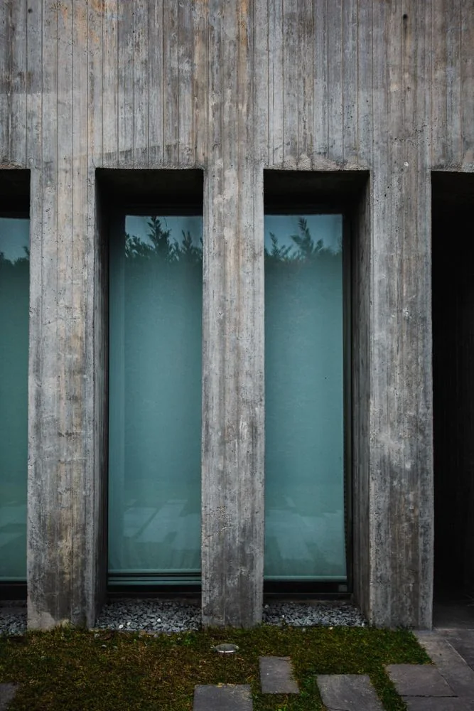 Contemporary concrete house facade with tall windows and textured walls.