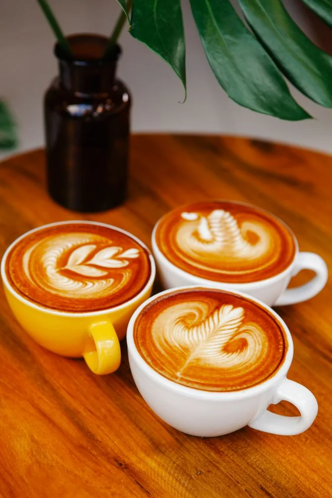 Three lattes with leaf-shaped foam art Three cups of latte with leaf-shaped foam art on a wooden cafe table.