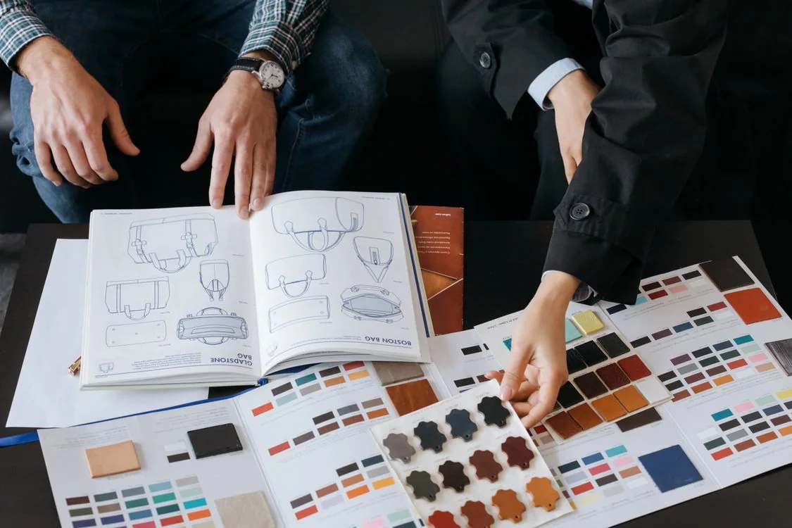 Designers' hands comparing color swatches beside product sketches at a studio table.