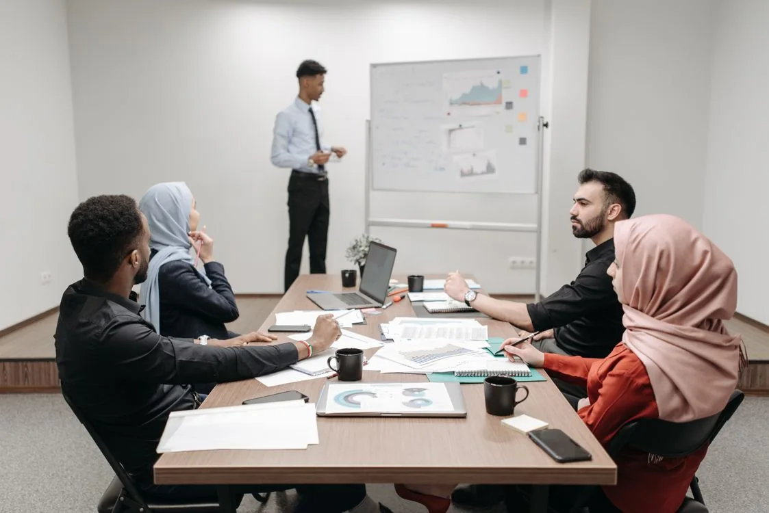 A consulting team discusses charts and documents around a meeting table.