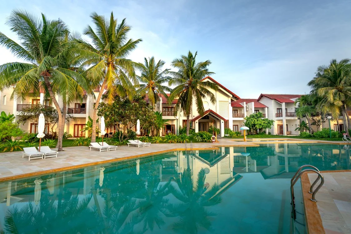 Palm trees and quiet guest villas reflected in a turquoise resort swimming pool.