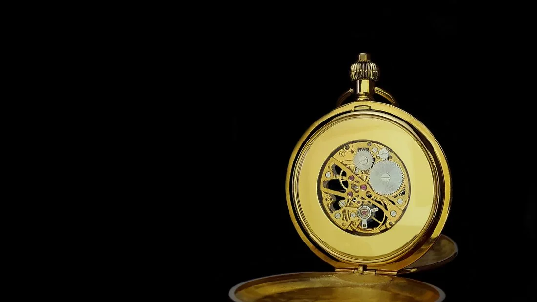 Open gold pocket watch showing its mechanical movement against black.