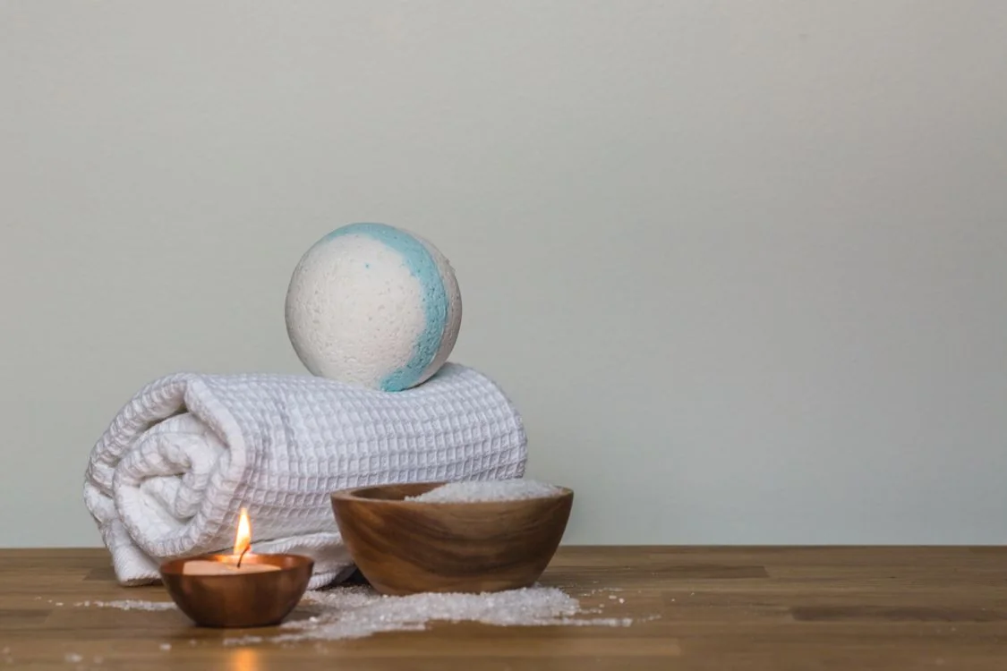 A bath bomb, folded towels, wooden bowl and candle in a calm spa arrangement.